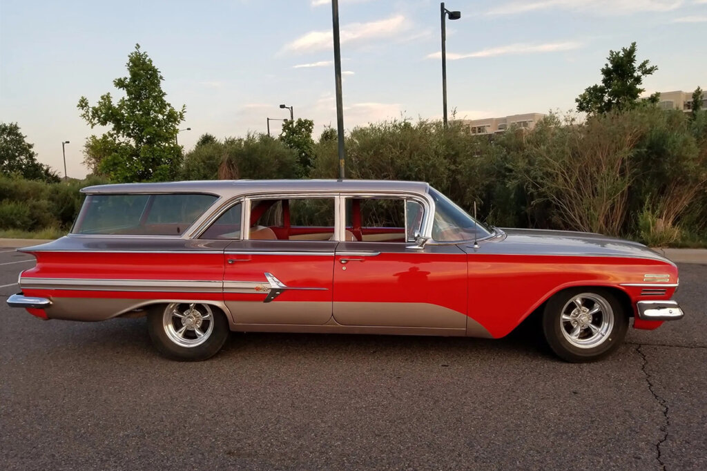 Side shot of a red and chrome Chevy nomad with 4 doors in a parking lot