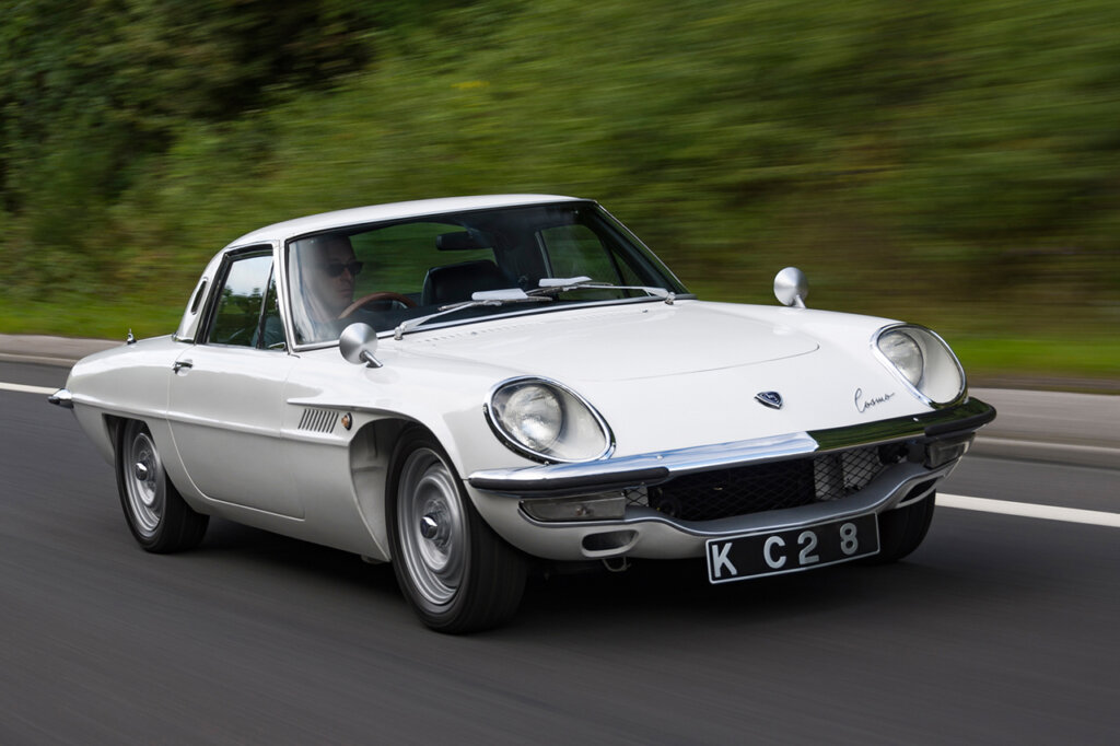 White Mazda cosmo passing greenery in background