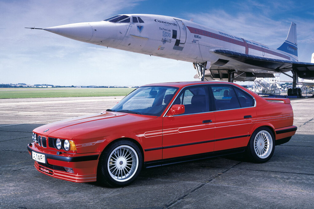 Red BMW Alpina 3-series parked next to a white airplane