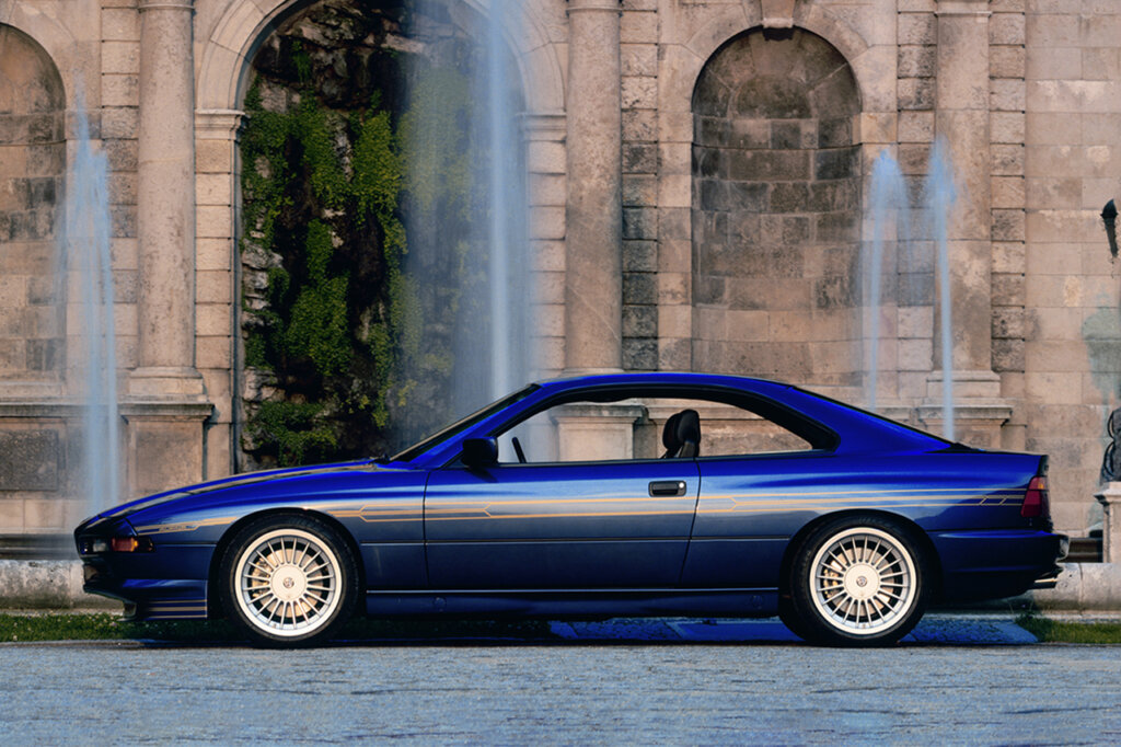 Side profile of a blue BMW 7-series parked with a large stone building behind it