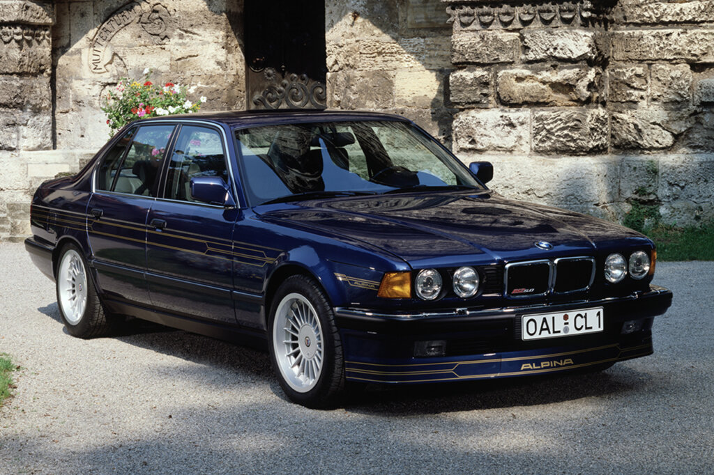 Blue BMW Alpina E32 B12 sedan parked in front of a stone structure