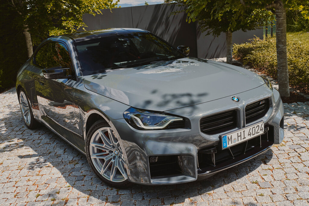 Grey BMW parked at an angle on a stone driveway with trees providing shade