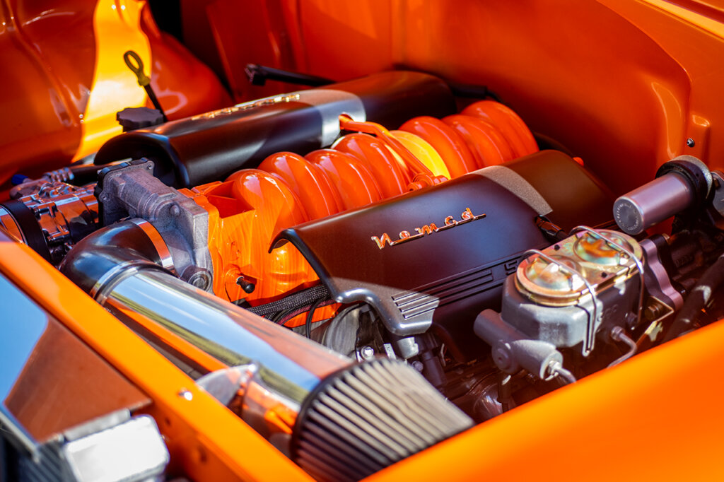 Orange intake with two black covers with words on them on top of an engine inside of an orange car