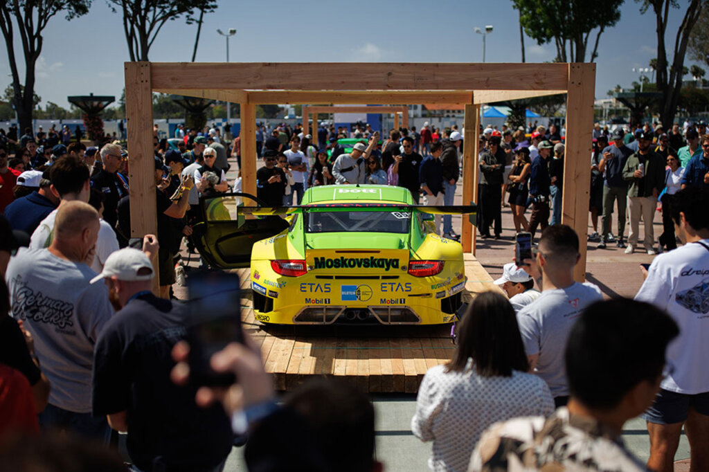 Yellow and green porsche staged on a wooden platform with a crowd of people surrounding it