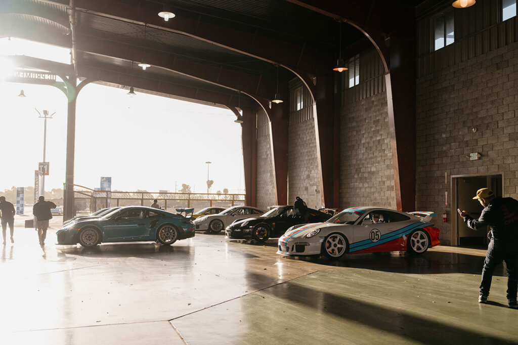 People near cars being parked inside of a brick building with a sun flare in the background