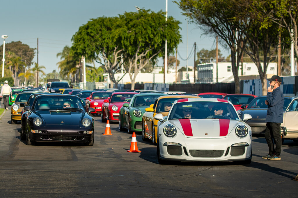 Porsche cars in two lines one black on the left and one on the white with red stripes with trees in the background