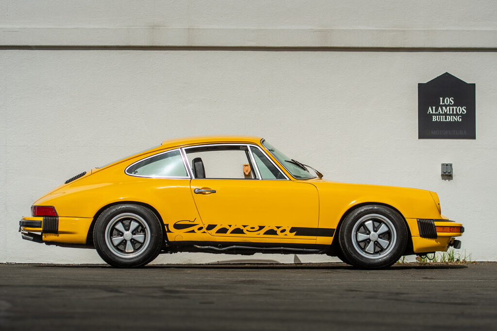 Yellow Porsche 911 Carrera parked near a white building with a black sign