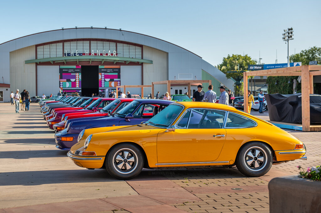 Yellow porsche 912 parked side by side other cars with a large warehouse in the background
