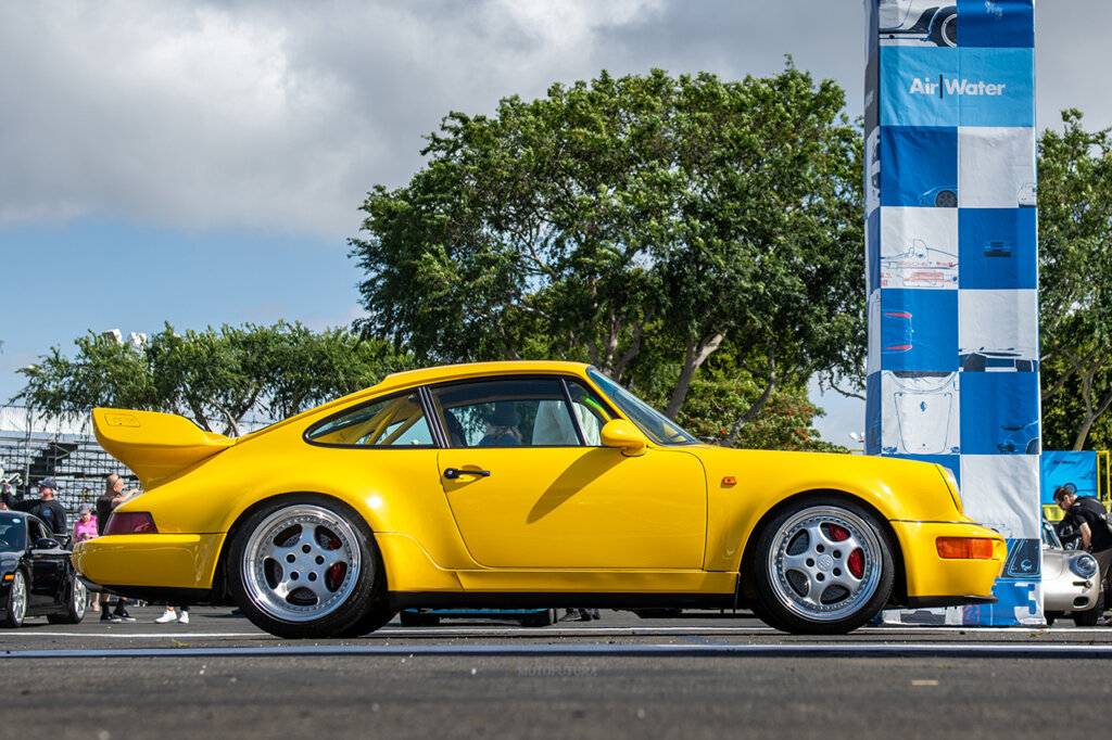 Yellow porsche 911 with a blue and white banner tower in background