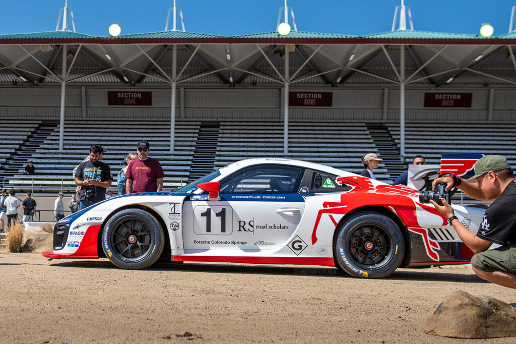 Porsche race car with a red and white paint job with a large wing staged in front of bleachers