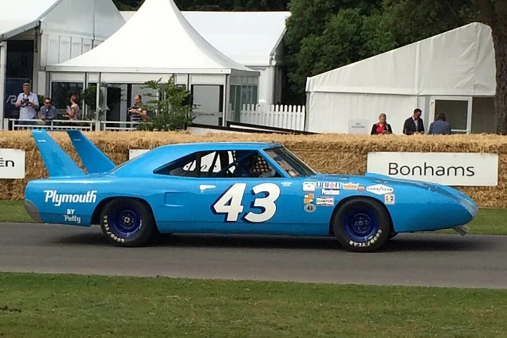 Side profile of the Petty Superbird driving on a pathway near grass and tents in background