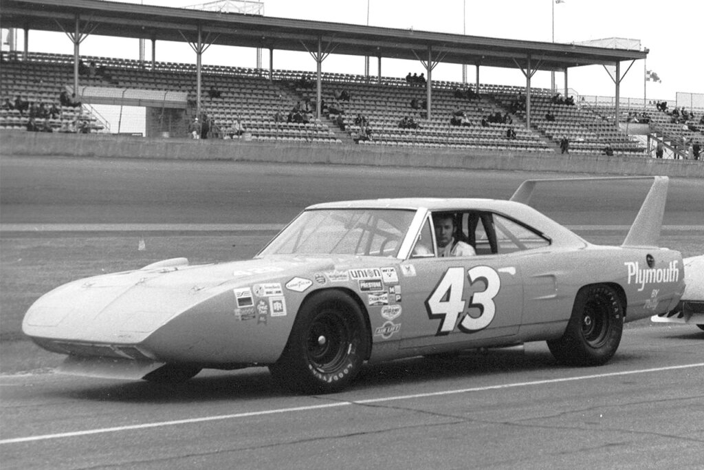 black and white photo of a Plymouth superbird driven on a race track with a man behind the wheel with the number 43 on the door