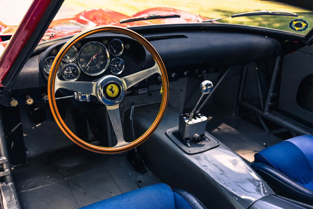 Interior shot of a wood grain steering wheel and metal gear shifter with blue leather seats
