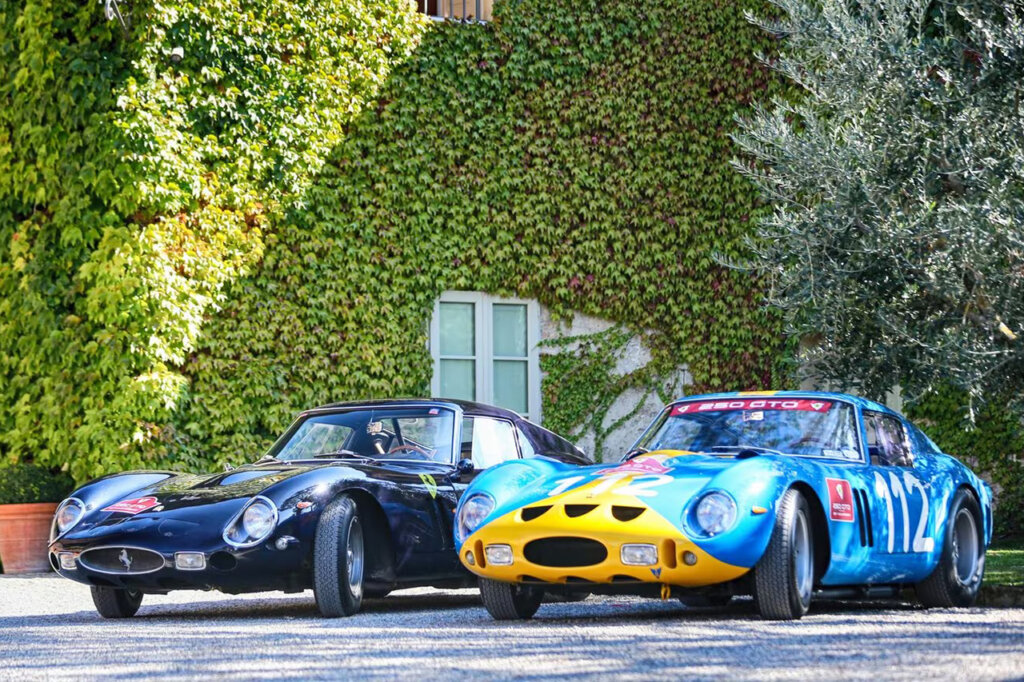 Two ferrari 250 GTO cars parked next to one another with a large plant covered wall and window behind these