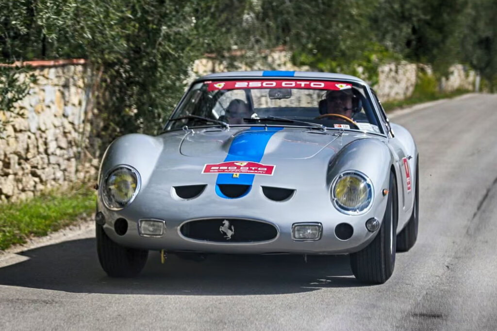 Silver Ferrari 250 GTO driving with a man behind the wheel on a road