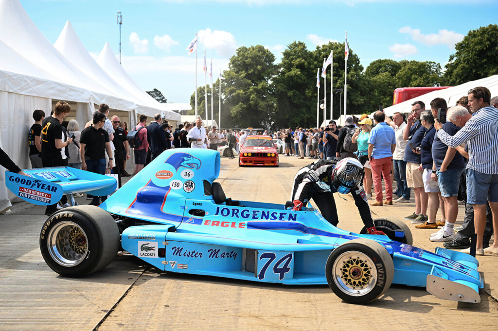 light blue race car with a man standing next to it with full race gear