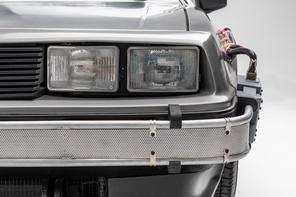 closeup of silver car with mesh grill bumper, exposed wiring & square headlights