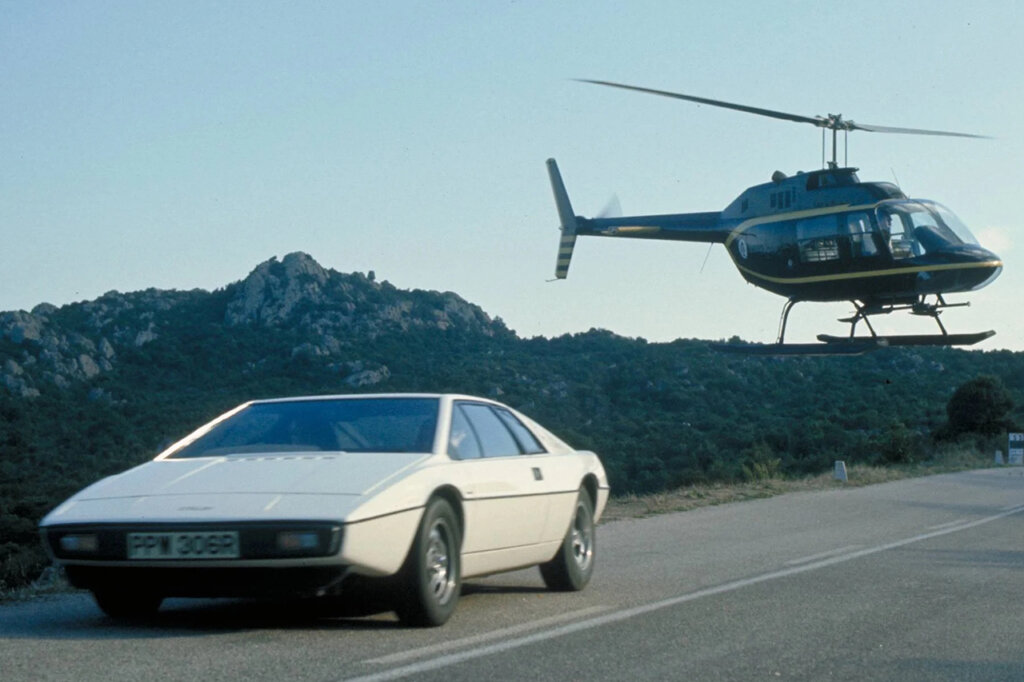 White car driving on the road with a helicopter following it closely