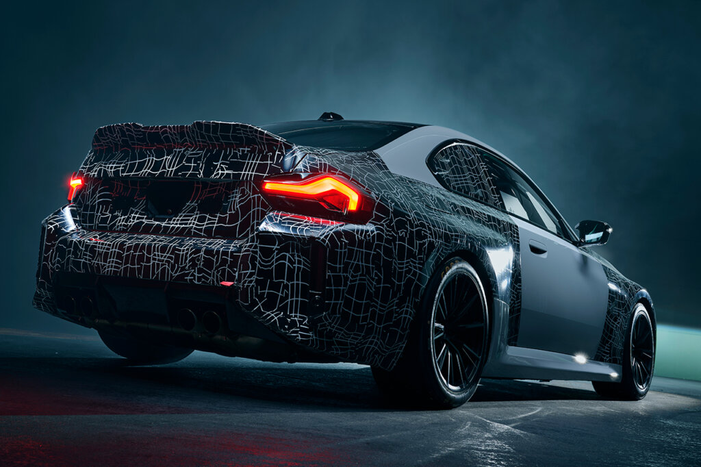 Rear end of a silver BMW parked in a room with smoke behind the car and its red taillights on