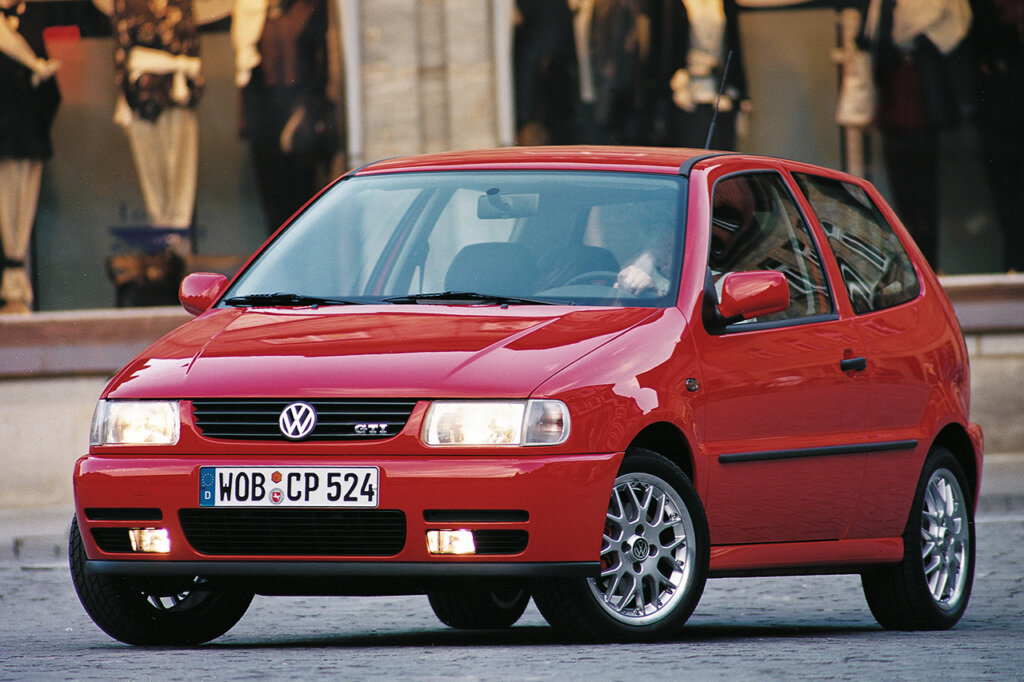 Red VW Polo GTI parked at an angle on brick road with store fronts behind the car