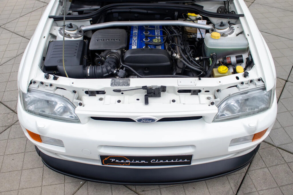 Engine bay with blue valve cover under a long silver horizontal bar inside of a white ford car
