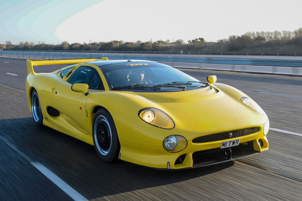Yellow Jaguar sports car driving fast on an open freeway with a railing behind it