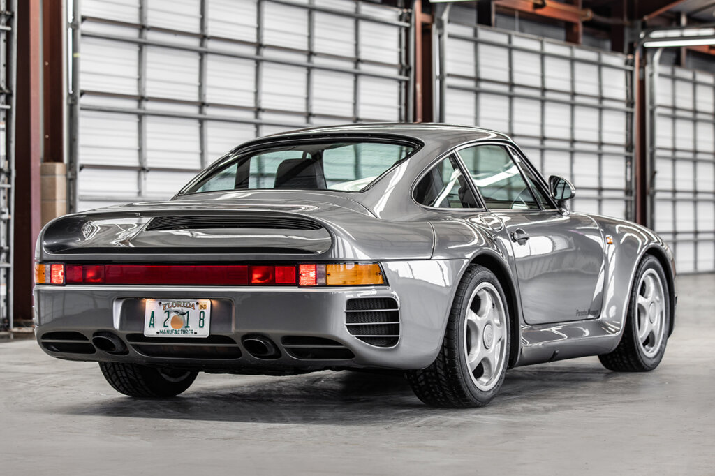 Rear side of the Porsche 959 with large horizontal rear taillight bar and vents with long sleek rear spoiler parked inside of a garage