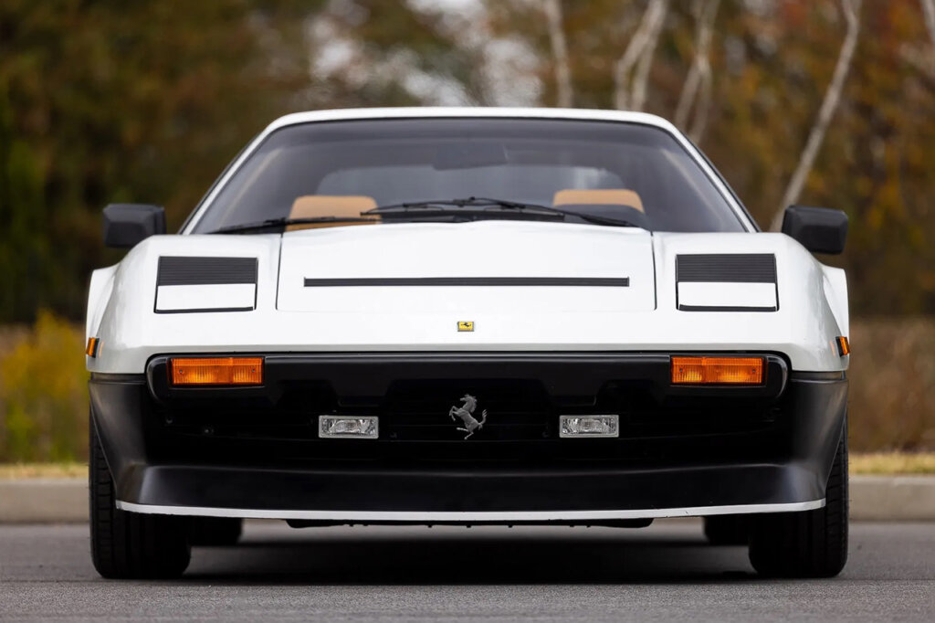 Front end of a white and black Ferrari with trees in background