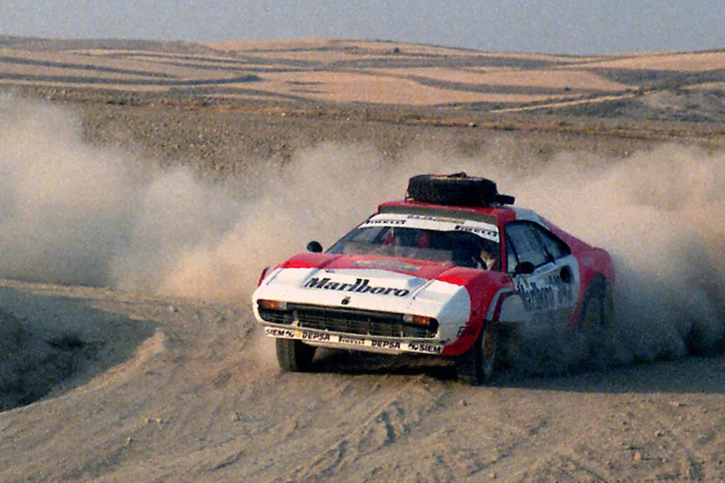 Red and white Marlboro livery Ferrari 308 drifting through a dirt course leaving cloud of smoke