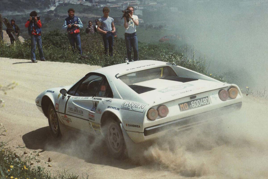 White rally racing Ferrari on a dirt track passing spectators in background