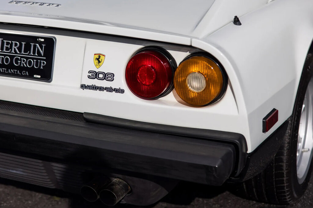 White car with red and amber taillight next to Ferrari 308 GTS badge