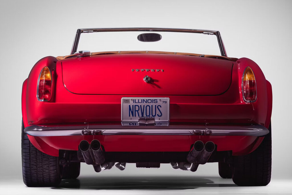 rear end of a red car with two small taillights with a thin chrome bumper in a white room