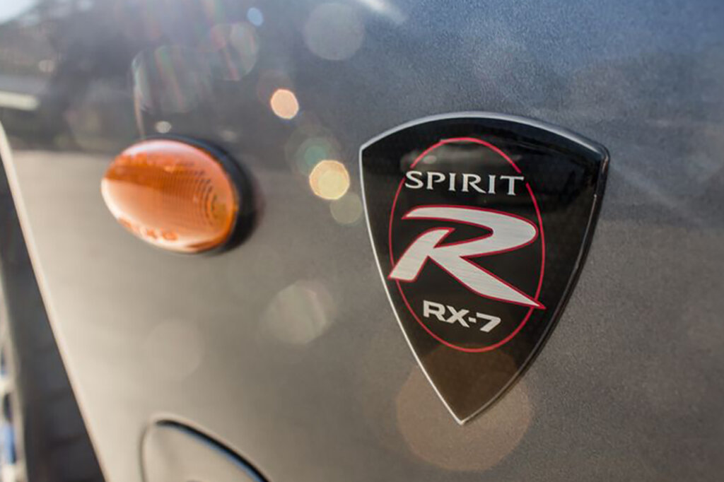 Triangular shield badge that says Spirit R RX7 next to a turn signal light