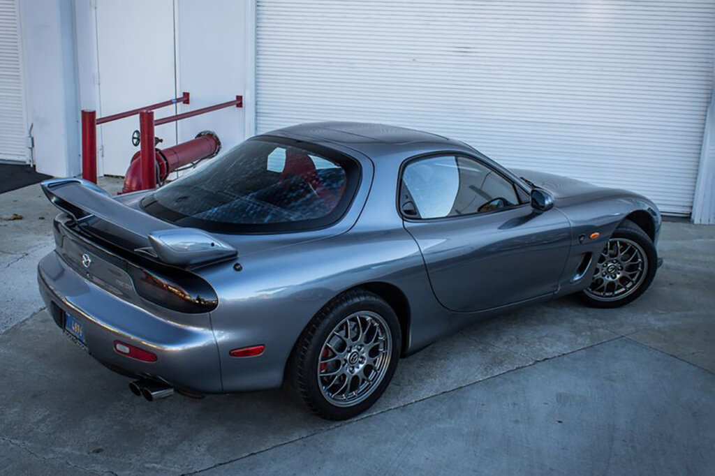 Grey Mazda RX7 Spirit R parked in front of a white garage door with red pipes behind it