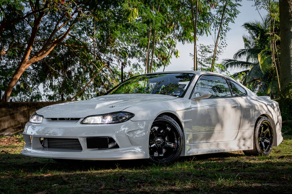 White Nissan Silvia S15 parked under some trees with the headlights on