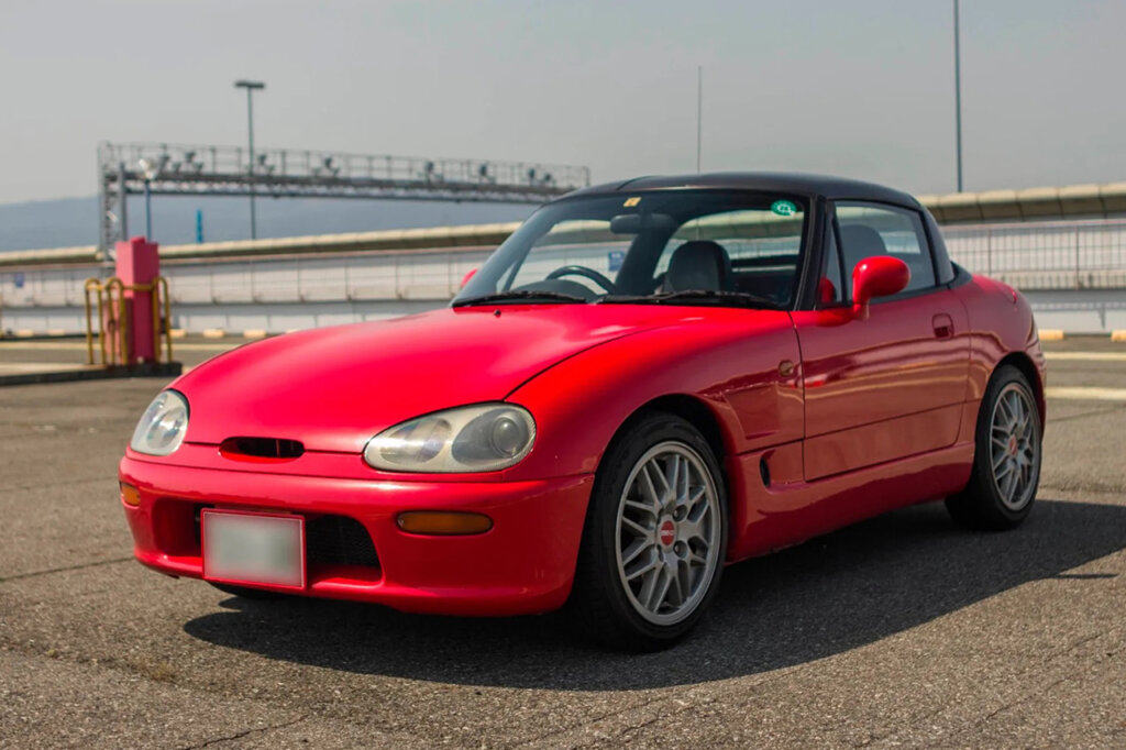 Red and black Suzuki Cappuccino parked on a road with concrete barrier in the background