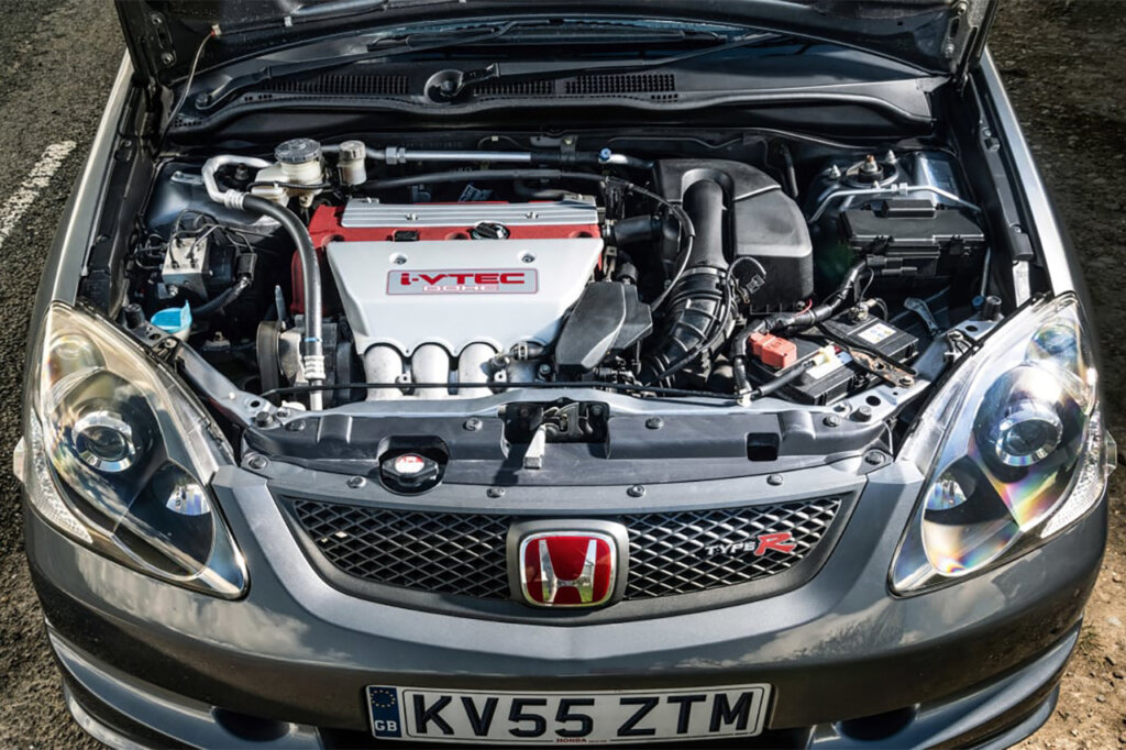 Silver car with red Honda badges and Type R on the front grill of a Honda civic with a silver and red valve cover on the engine