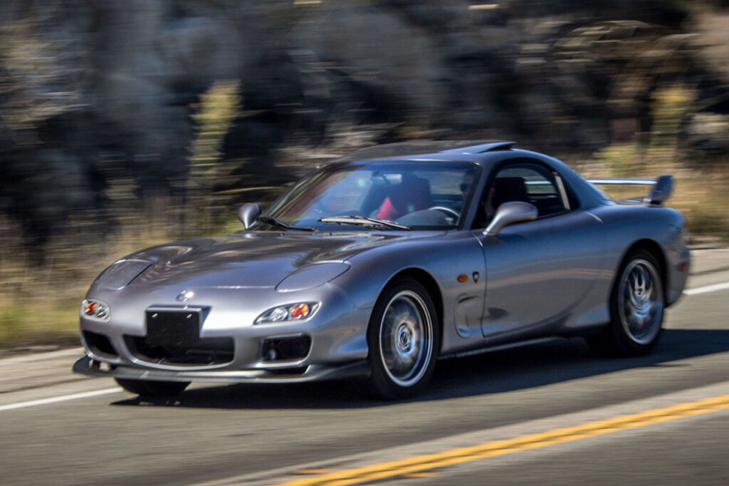 Grey Mazda RX7 Spirit R driving through a canyon passing rocks driving on an asphalt road