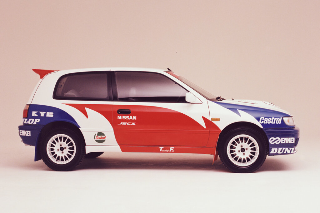 Blue white and red Nissan GTi-R Pulsar parked sideways in a white room with a pink background behind it