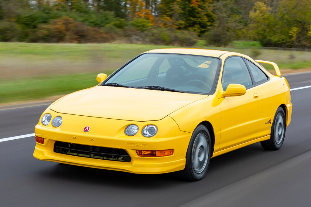 Yellow DC2 integra Type R driving fast on the road passing grass and trees in the background