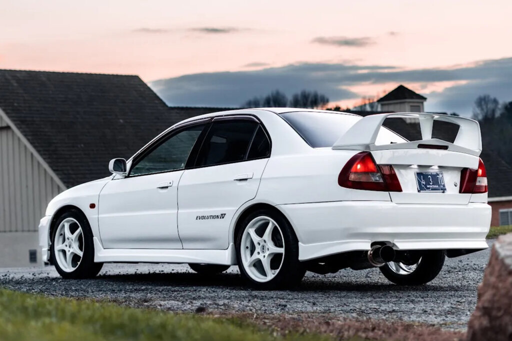 White Lancer Evo IV GSR parked in front of a building with the sun setting in the sky in the background