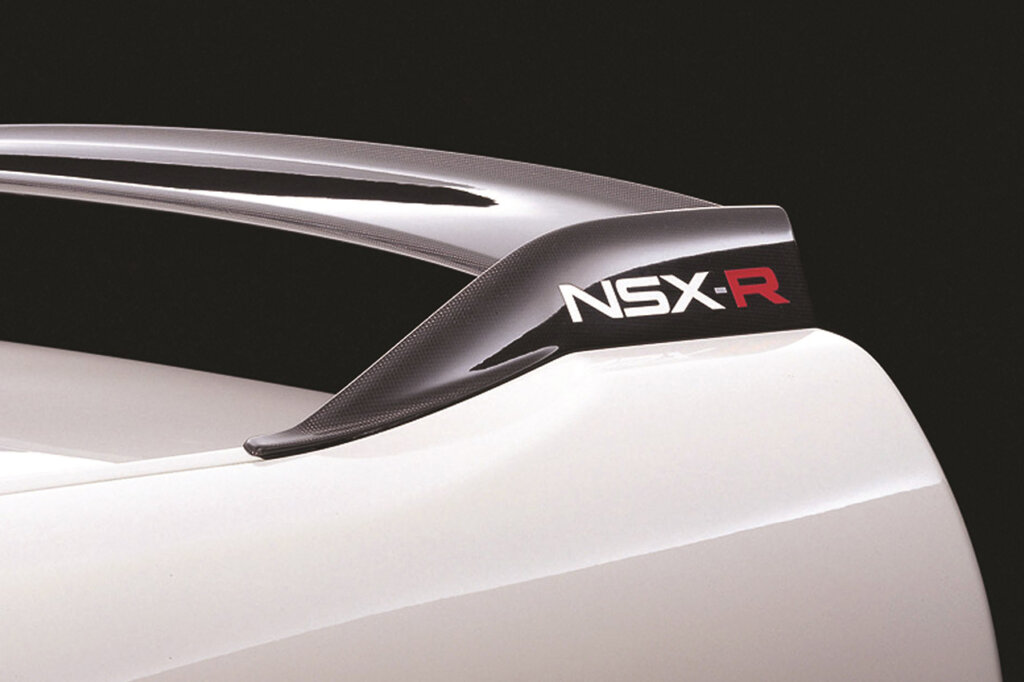 Black badged rear spoiler wing of a white Honda NSX-R with black background behind the car