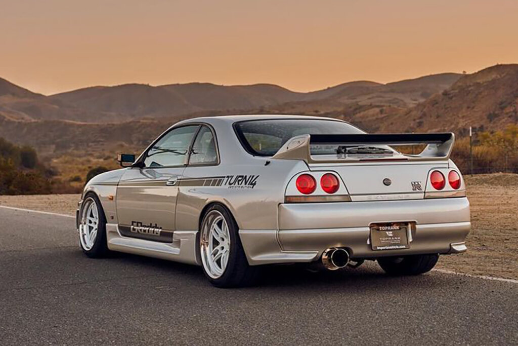 Silver R33 Skyline with decals on the side of the car parked with the sun setting behind mountains in the background