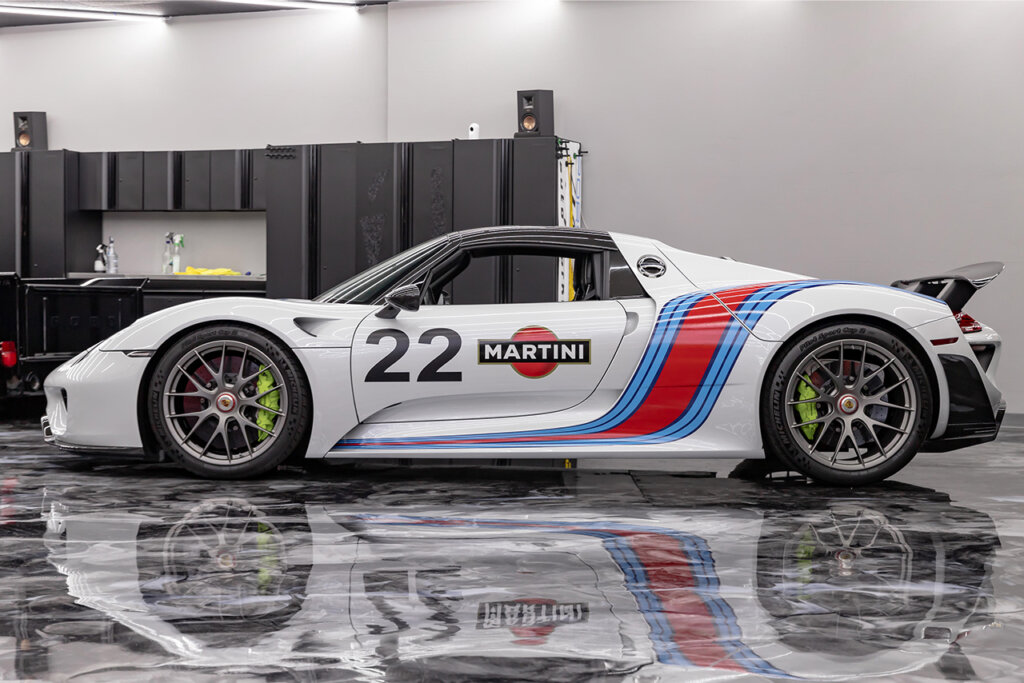 Side profile of Martini Porsche 918 car pictured in a garage with the reflection of the car below it
