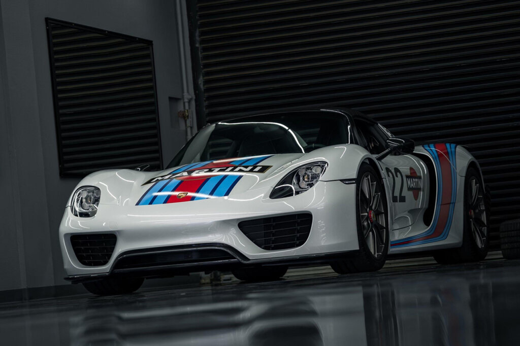 White Porsche 918 with red and blue stripes on hood in a dark room