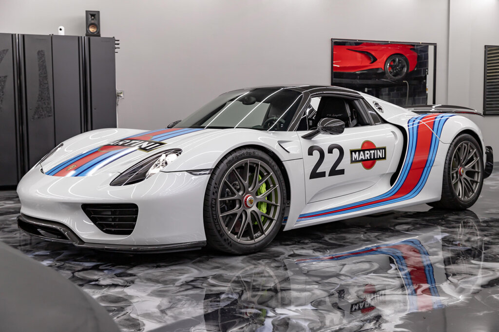 White Porsche 918 with red and blue stripes and the number 22 on the door parked in a garage with marble swirl floor