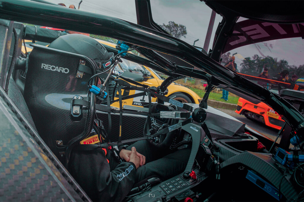 Recaro racing seat with multiple safety points and harnesses attached to it with a man in racing gear sitting in the seat