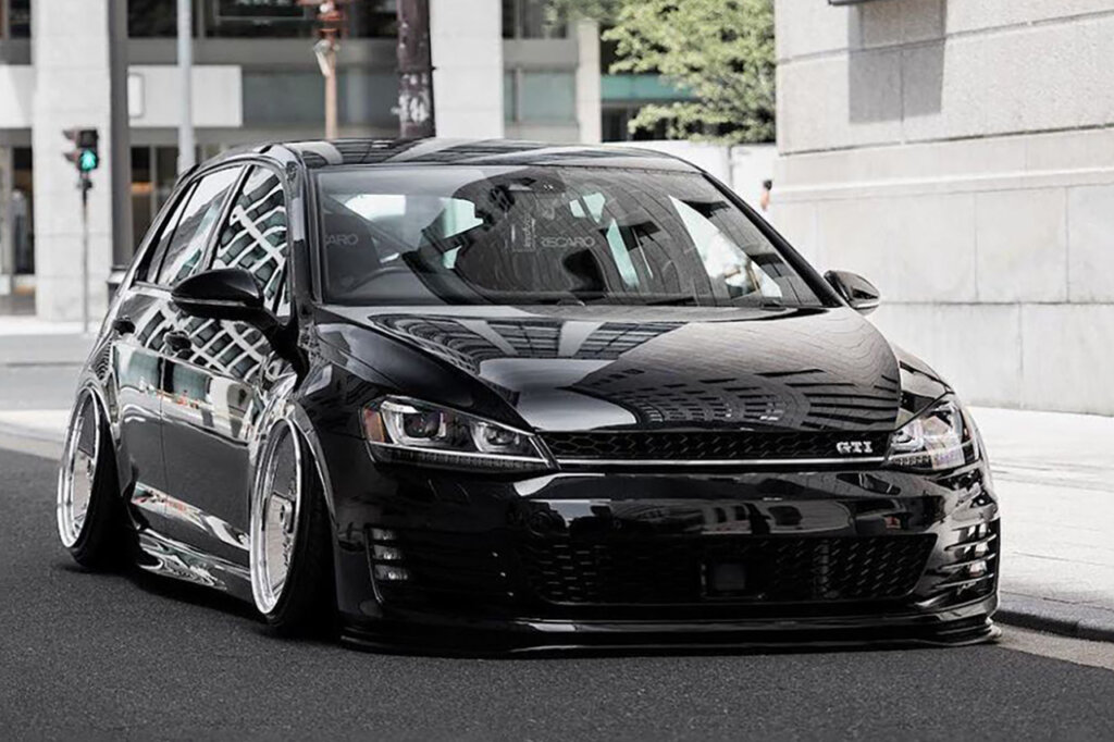 Black VW car parked next to a sidewalk in a cityscape background