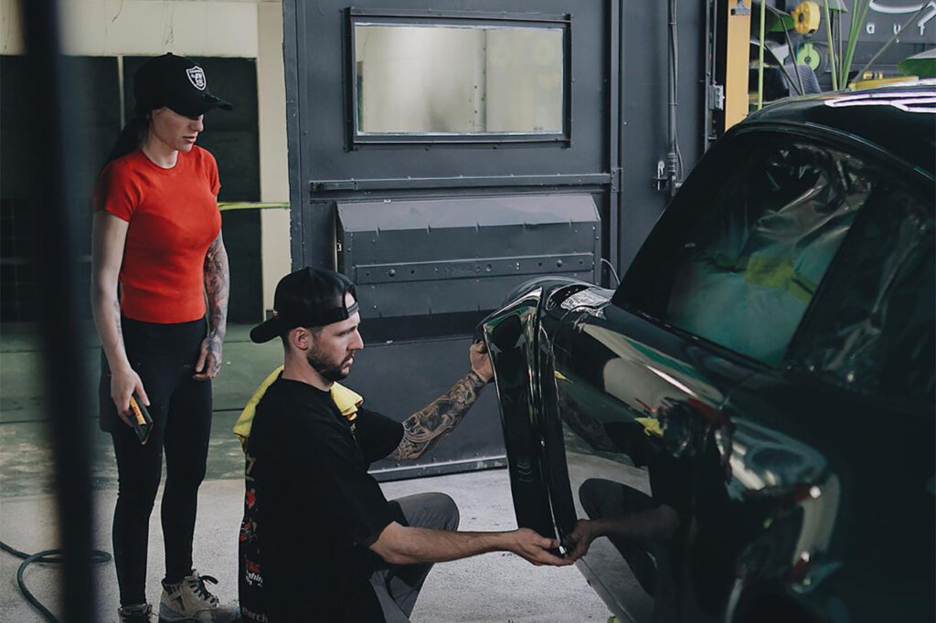 Two people standing and working on a Green Porsche car inside of a garage