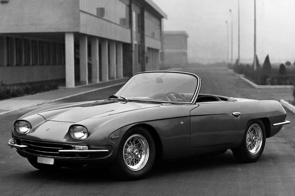 Black and white photo of a Lamborghini 350 GTS parked in front of a building and an empty road